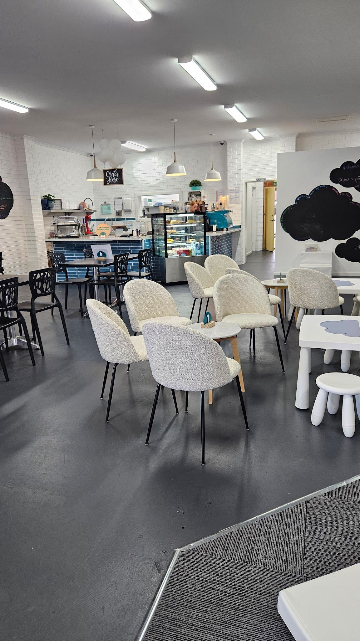 Four C's Cafe interior with white brick walls, blue-tiled counter, cream boucle chairs and pendant lights