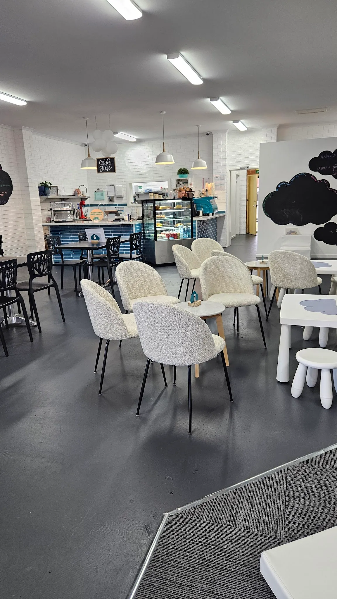 Four C's Cafe interior with white brick walls, blue-tiled counter, cream boucle chairs and pendant lights