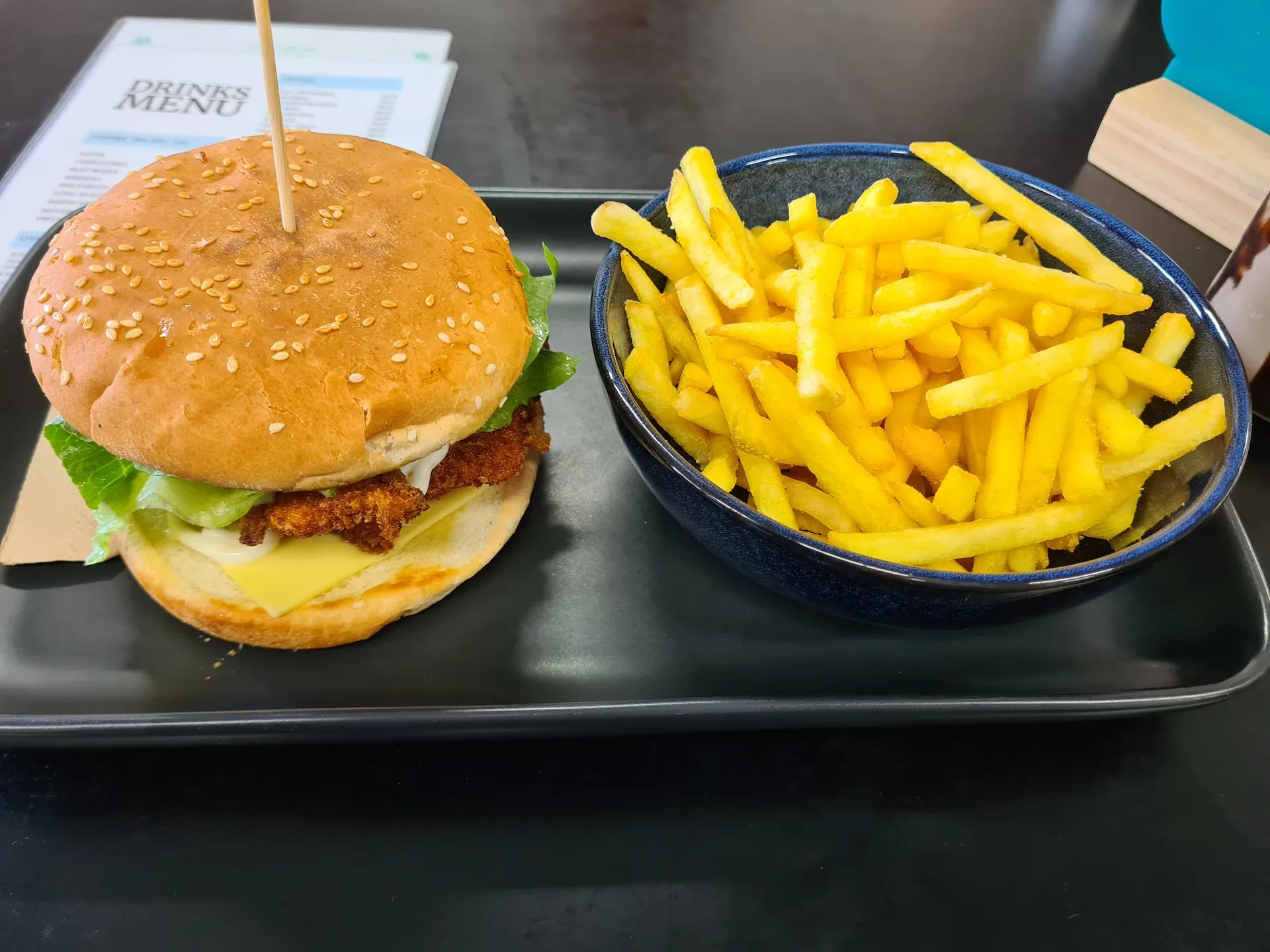 Crispy chicken burger with fries in blue ceramic bowl on black tray