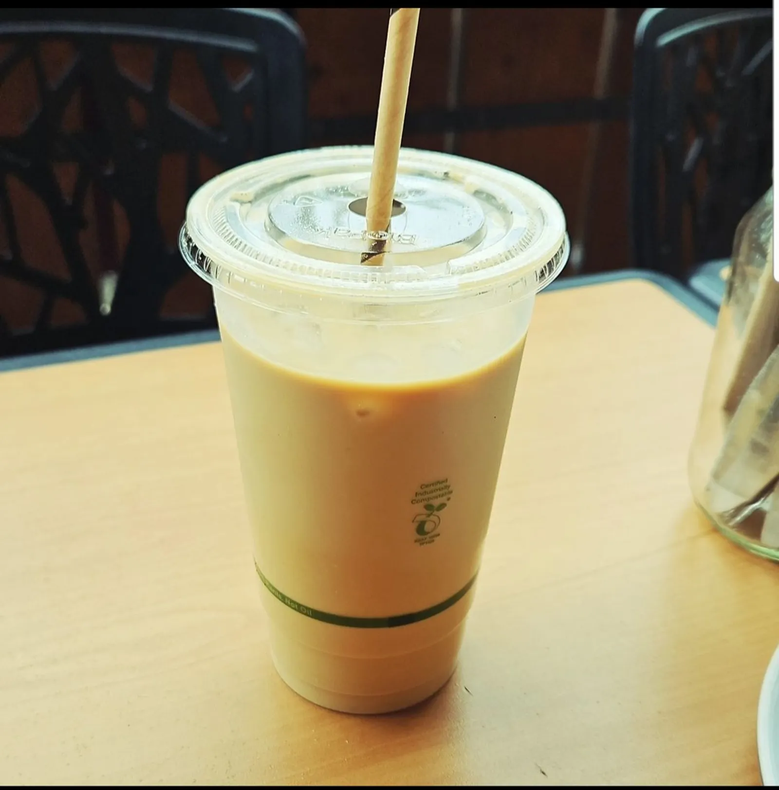 Iced latte in clear plastic cup with paper straw on wooden table