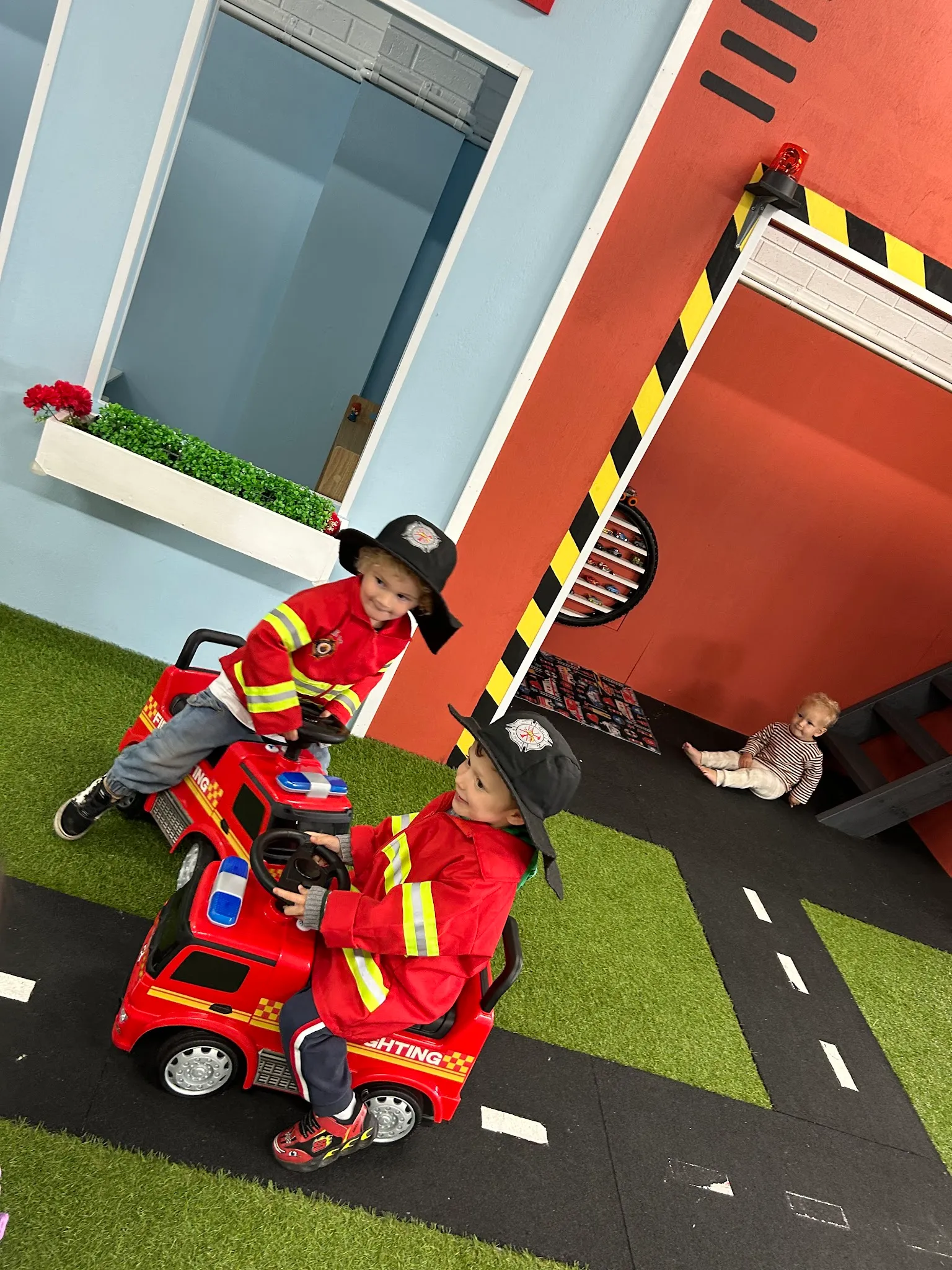 Two children in firefighter costumes riding electric fire truck in Four C's Cafe play zone