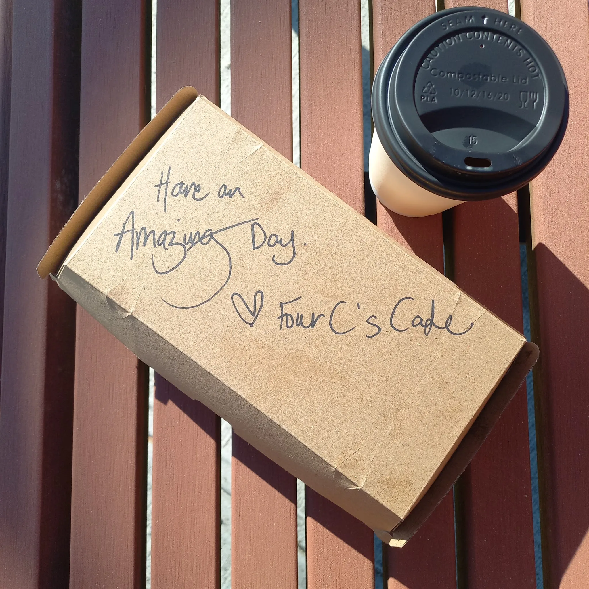 Four C's Cafe takeaway box with handwritten 'Have an Amazing Day' message and coffee cup